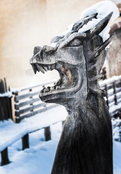wooden sculpture depicting a dragon, mouth wide open, covered in snow