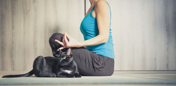 woman doing yoga at home - black cat sitting next to her