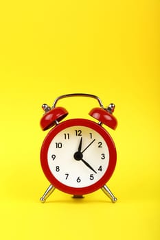 Close up one small red metal twin bell retro alarm clock over yellow paper background with copy space, low angle front view