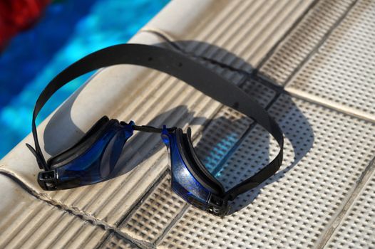 Blue goggles for swimming on a side of the swimming pool