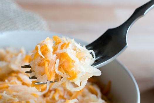 Fermented cabbage and carrots on a fork above a bowl