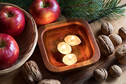 Christmas decoration - apples, pine branches, walnuts and floating candles made from nutshells in a bowl of water