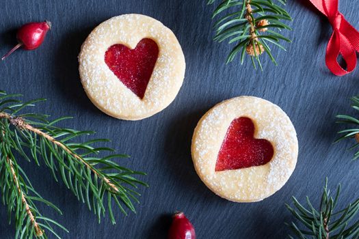 Christmas background with two Linzer Christmas cookies, dried rose hips and spruce branches