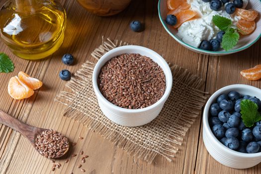 Flax seeds in a bowl, with cottage cheese, oil and fresh blueberries in the background