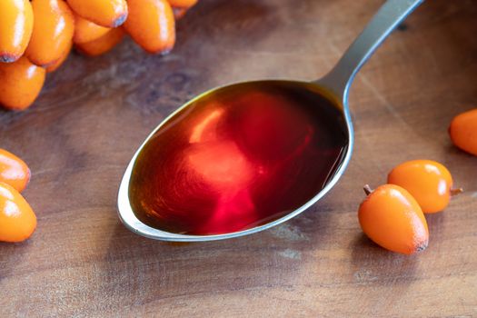 Sea buckthorn oil on a spoon with fresh berries
