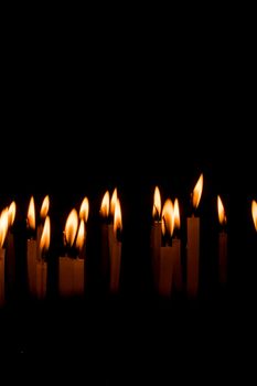 Many christmas candles burning at night on the black background. Candle flame set isolated in black background. Group of burning candles in dark with shallow depth of field. Close-up. Free space.