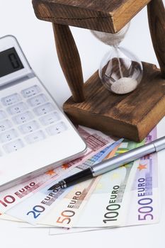 Different euro banknotes with hourglass white calculator and fsilver founten pen on white background