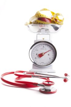 Red stethoscope with Red apple and  yellow measuring tape on kitchen scale isolated on white