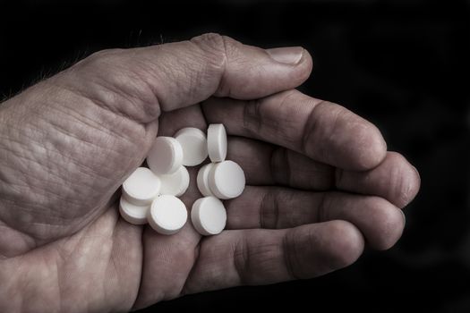 Old dirty hand with round white pills on black background