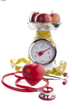 Red apple with  yellow measuring tape on kitchen scale with red heart and stethoscope isolated on white