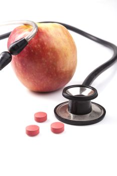 Red Apple with black stethoscope and red pills with reflection isolated on white background