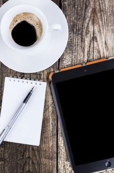 Morning coffee with a spiral notepad and fountain-pen and a tablet on old brown dood background