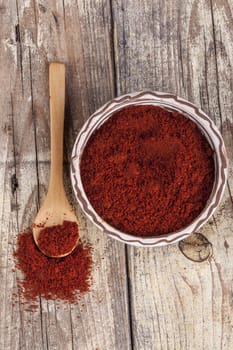 Red paprika in a ceramic bowl with brown wood spoon on old wood table