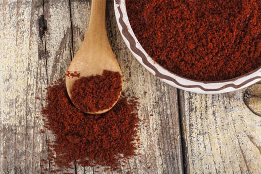 Red paprika in a ceramic bowl with brown wood spoon on old wood table