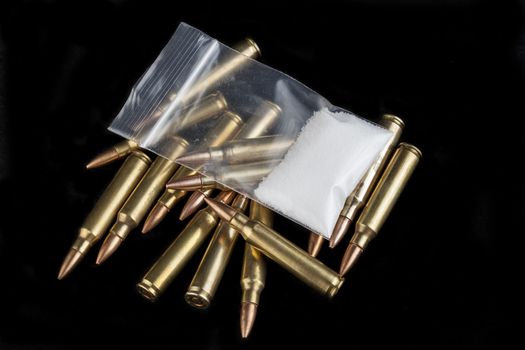 Rifle bullets close-up on black background with a bag of white drug powder