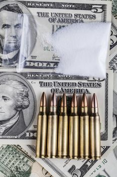 Bullets on dollar banknotes with bag of white drug powder on black background