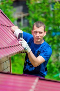 vertical portrait of a man with a hammer repairing the roof of the house, shooting outdoors