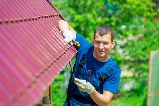 A young man repairs the roof of the house in overalls with a tool