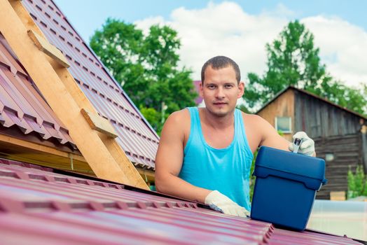 Portrait of a man with a toolbox on the roof of the house during the repair