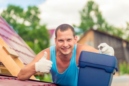 joyful man with a toolbox on the roof of the house during the repair