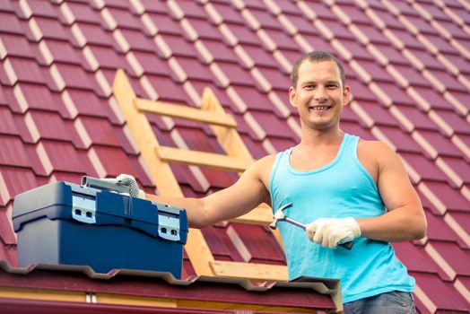 happy portrait of a man with a toolbox on the roof of the house during the repair on the background of roof tiles