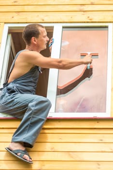 Male professional in overalls cleans the window in the house