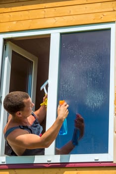 Portrait of a man in overalls with spray washes a window in the house