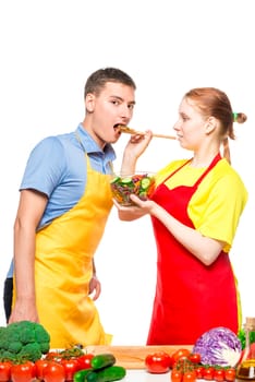 wife treats a man to a fresh vegetable salad, a pair of aprons on a white background