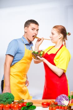 wife treats a man with fresh vegetable salad, a pair of aprons in the kitchen