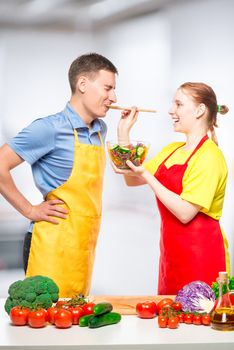 girl treats her lover with fresh vegetable salad, which they cooked together in the kitchen