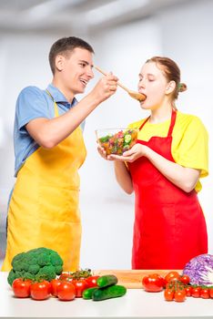 a man treats a girl with fresh vegetable salad, which they cooked together in the kitchen