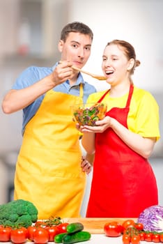 a man with a wooden spoon feeds a girl with a useful vegetable salad in the kitchen