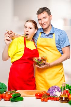 young couple in the kitchen posing with vegetable salad in a bowl