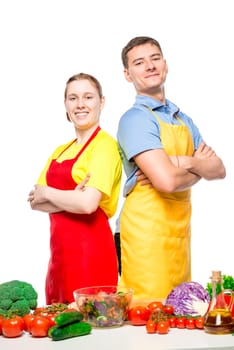 happy man and woman in aprons preparing salad from vegetables, portrait on white background