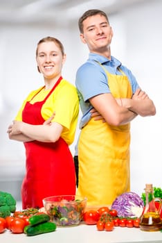 happy man and woman in aprons preparing vegetable salad, portrait in the kitchen