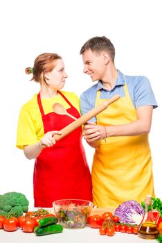 couple fighting with kitchen utensils while cooking salad on white background