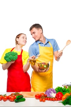 A young couple looks at each other in love while cooking vegetable salad on a white background