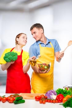 A young couple looks at each other in love while cooking vegetable salad in the kitchen