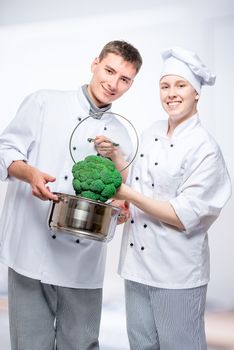vertical portrait of fellow cooks with saucepan and broccoli in a commercial kitchen