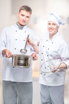successful professional chefs with a pan and a ladle in a commercial kitchen posing