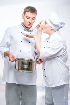 two cooks in suits try the cooked soup in the commercial kitchen