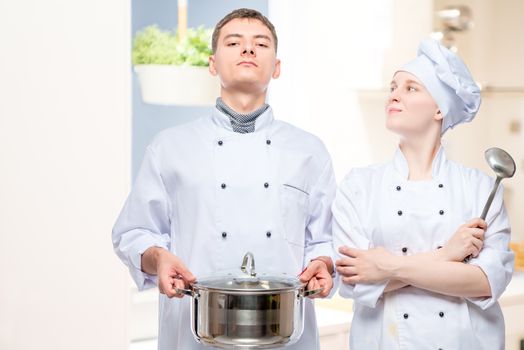 portrait of a man and a woman in cook suits posing with a pan on the background of the restaurant’s kitchen