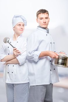 cooks in suits with a saucepan and a ladle posing against the backdrop of a commercial kitchen