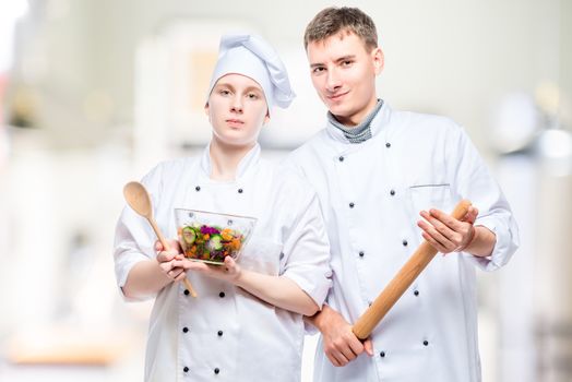 portrait of professional couple of cooks with salad and rolling pin on the background of commercial kitchen