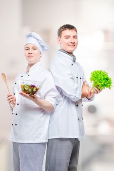 professional happy chefs in suits with a salad in their hands against the background of the kitchen