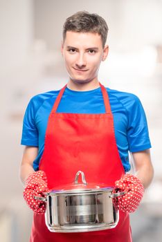 male cook in an apron holding a pot in his hands, portrait in the kitchen