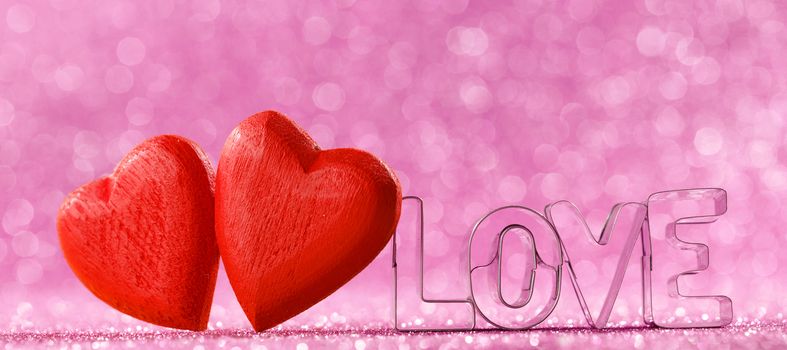 Two red handmade wooden hearts and word love on pink bright glitter lights bokeh background