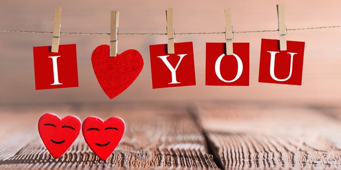 Clothes pegs and I LOVE YOU words on papers on rope on wooden background with hearts Valentines day concept