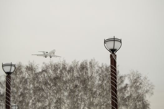 The plane flies low over the city Park and trees, cloudy winter sky. Copy space business travel adventure concept.