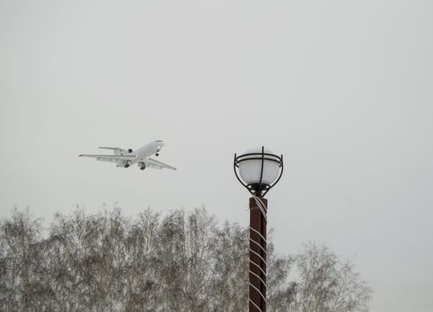 The plane flies low over the city Park and trees, cloudy winter sky. Copy space business travel adventure concept.
